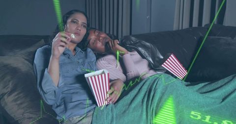 Cuddling couple watching movie on sofa sharing popcorn under cozy blanket with data overlay