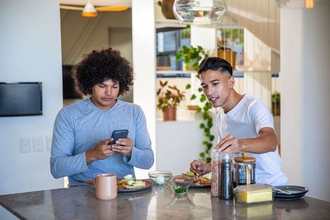 Two friends sharing breakfast while using smartphone