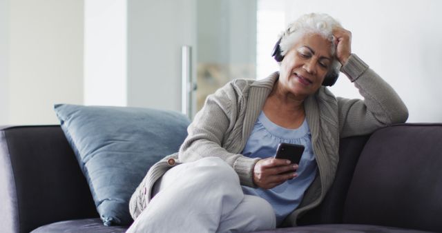 African american senior woman wearing headphones using smartphone sitting on the couch at home. retirement senior lifestyle living in quarantine lockdown concept