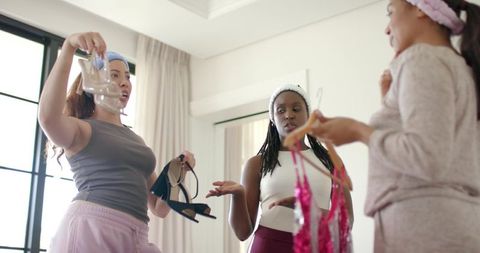 African american women trying on lucite heels, black sandals and pink sequined dresses in bedroom