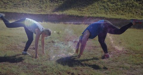Two women balancing in park during golden hour lens flare fitness stretching duo