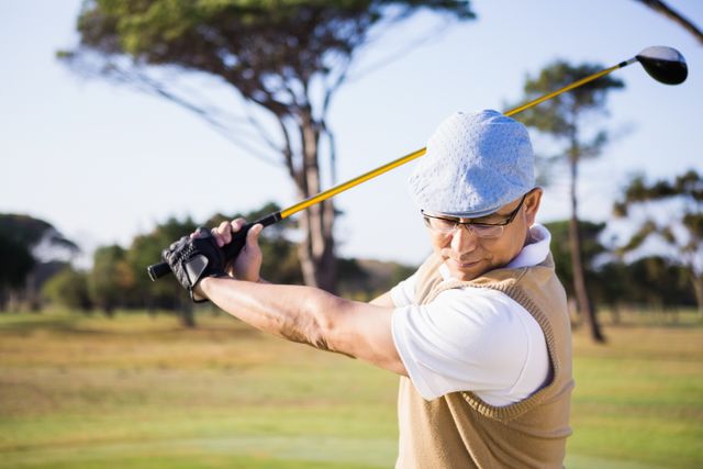 Senior man swinging golf club on a sunny day at a golf course. Ideal for promoting active lifestyles, senior fitness, outdoor sports, and leisure activities. Suitable for use in advertisements, sports magazines, and health and wellness campaigns.