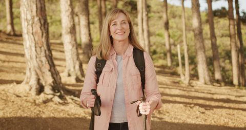 Smiling Senior Woman Hiking in Sunny Forest with Walking Poles