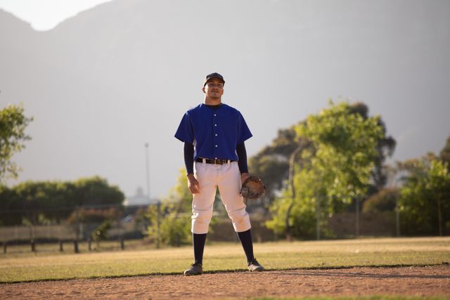 Biracial male baseball fielder standing on a sunny day in a baseball field, wearing a glove and uniform. Ideal for use in sports-related content, advertisements for athletic gear, or articles about baseball and outdoor activities.