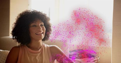 Smiling woman enjoying sunlit living room with colorful particle cloud