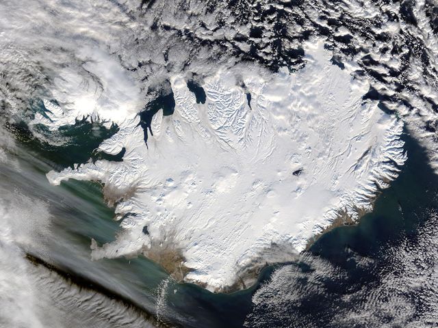 Iceland, dressed in winter white, peaked through a hole in a complex system of clouds in late February, 2015. The Moderate Resolution Imaging Spectroradiometer (MODIS) aboard NASA’s Terra satellite captured this true-color image on February 21 as it passed over the region.  Ice and snow covers Iceland almost entirely, except for coastal regions in the southwest and southeast. The extensive, roughly H-shaped area in the southeast section of the island is Vatnajökull, Iceland’s largest glacier. Hidden underneath the ice lies Bardarbunga, a large subglacial stratovolcano. On August 31, 2014 the volcano began an eruption at two fissures to the north of the glacier and deposited a lava field that measured about 131 feet (40 meters) at its thickest points, and covered an area about 33 sq. mi (85 sq. km) by the time the eruption ended on February 27, 2015. The massive lava flow left its mark on Iceland – the cooled lava can be seen as the roughly oval black area to the north of the Vatnajökull glacier.  Credit: NASA/GSFC/Jeff Schmaltz/MODIS Land Rapid Response Team  <b><a href="http://www.nasa.gov/audience/formedia/features/MP_Photo_Guidelines.html" rel="nofollow">NASA image use policy.</a></b>  <b><a href="http://www.nasa.gov/centers/goddard/home/index.html" rel="nofollow">NASA Goddard Space Flight Center</a></b> enables NASA’s mission through four scientific endeavors: Earth Science, Heliophysics, Solar System Exploration, and Astrophysics. Goddard plays a leading role in NASA’s accomplishments by contributing compelling scientific knowledge to advance the Agency’s mission. <b>Follow us on <a href="http://twitter.com/NASAGoddardPix" rel="nofollow">Twitter</a></b> <b>Like us on <a href="http://www.facebook.com/pages/Greenbelt-MD/NASA-Goddard/395013845897?ref=tsd" rel="nofollow">Facebook</a></b> <b>Find us on <a href="http://instagram.com/nasagoddard?vm=grid" rel="nofollow">Instagram</a></b>