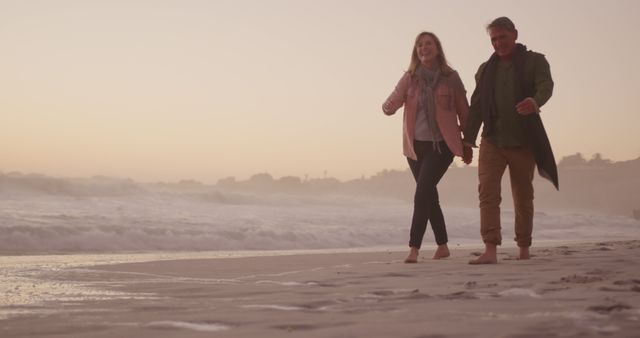 Happy senior caucasian couple holding hands walking on beach at sundown, copy space. Relationship, retirement, romance, vacations, nature, wellbeing and active senior lifestyle, unaltered.
