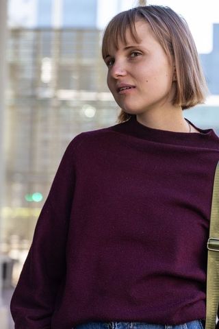 Young woman posing in maroon sweater glancing left urban streetstyle portrait
