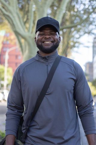 Smiling african american man wearing cap and crossbody bag on urban sidewalk
