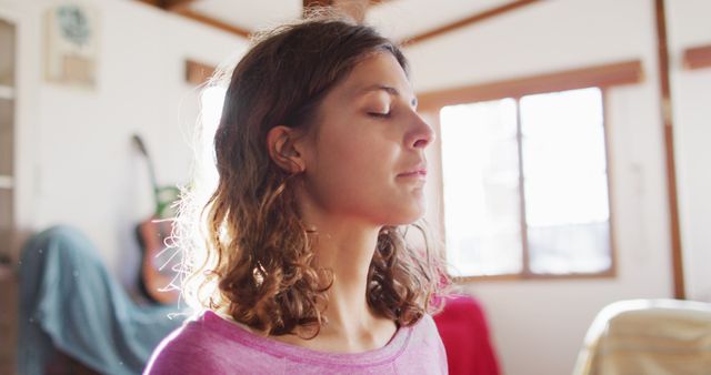 Woman meditating indoors with closed eyes, focusing on relaxation and mindfulness. This image captures a moment of serene calm, perfect for promoting wellness, mental health awareness, or illustrating concepts of relaxation techniques. Ideal for use in blogs, articles, or social media campaigns about meditation, self-care, and mental well-being.