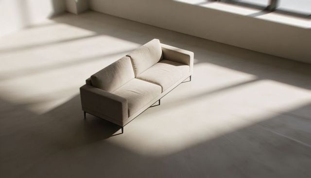 Minimal beige sofa on thin metal legs in sunlit loft with dramatic window shadows