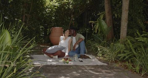 Relaxing couple enjoying shaded tropical garden picnic on sunlit patio