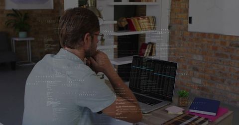 Developer analyzing code on laptop in modern home office with brick wall and notebooks