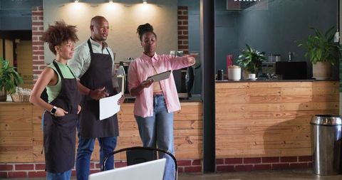 African american coffee shop team reviewing orders with tablet and paper at counter planning shift