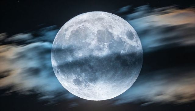Blue-Tinted Full Moon Showing Crater Detail with Wispy Clouds Passing Across Night Sky