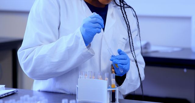 Scientist wearing gloves conducting an experiment using pipette and test tubes in laboratory. This image can be used for topics related to scientific research, medical tests, laboratory procedures, and biotechnology advancements. Ideal for illustrating concepts in healthcare facilities, scientific studies, academic journals, and laboratory environments.