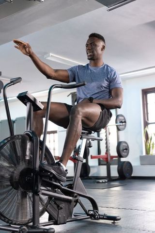 African american man pedaling and gesturing on air bike in modern gym for intense cardio
