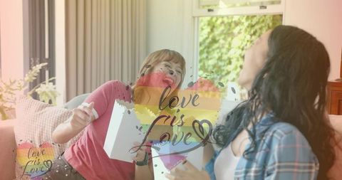 Smiling women opening gift on cozy living-room sofa with rainbow heart love is love