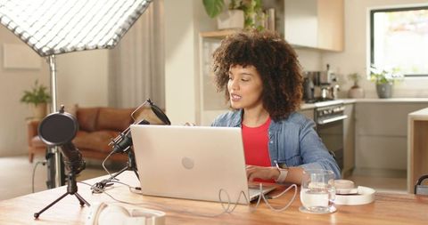 Female creator recording podcast in home kitchen studio with laptop mic and led light