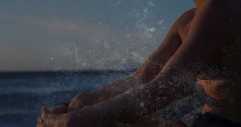 Woman sitting on shore at dusk hugging knees facing ocean horizon with grainy texture