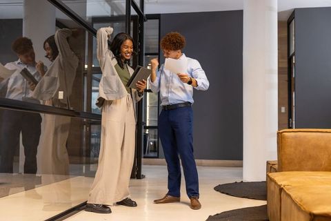 Celebrating office success: diverse coworkers reviewing results with tablet and documents