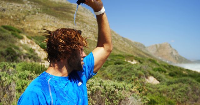 Man pouring water over his head to cool off while hiking in mountainous terrain. Useful for promoting outdoor activities, summer adventures, hydration awareness, and encouraging active lifestyles in nature.
