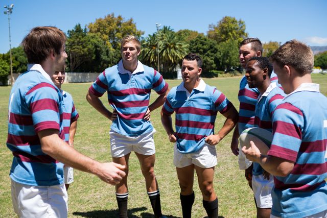 Rugby players in uniforms standing in a huddle on a sunny day, discussing strategy and game plan. Ideal for use in sports-related articles, teamwork and communication concepts, athletic training materials, and promotional content for rugby events or sports teams.