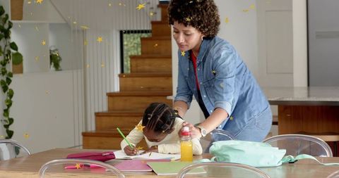 Mother guiding daughter with homework at kitchen table, denim shirt, family learning moment