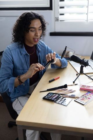 Non-binary creator recording makeup tutorial with cosmetics, brushes and microphone