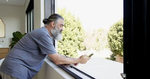 Senior Man Enjoying Tranquil Morning with Smartphone by Window