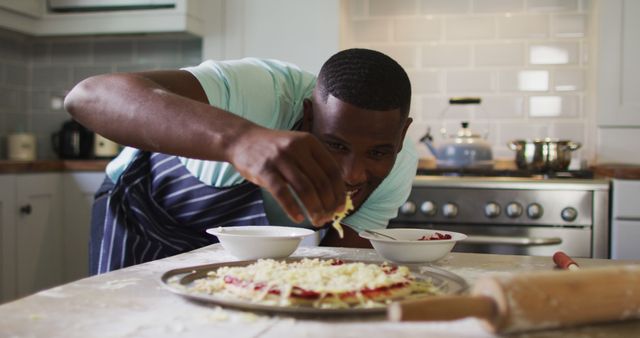 Home chef preparing a delicious homemade pizza, sprinkling cheese on top. Ideal for content related to cooking, culinary arts, hobby chefs, home-cooked meals, or kitchen appliance advertisements.