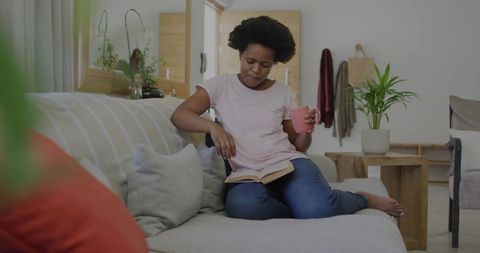 Afro woman sitting comfortably reading enjoyably with pink cup