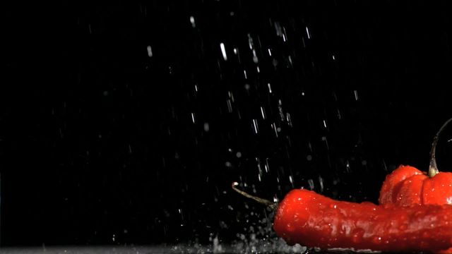 Red chili peppers being soaked in slow motion with water splashing against a dark background. This can be used for culinary websites, food blogs, advertisements for fresh produce, or artistic food photography promotions.