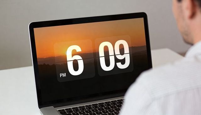 Man wearing striped shirt checking flip clock on laptop at minimalist home office desk
