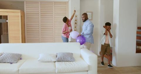 African American family decorating living room for birthday party holding purple balloons