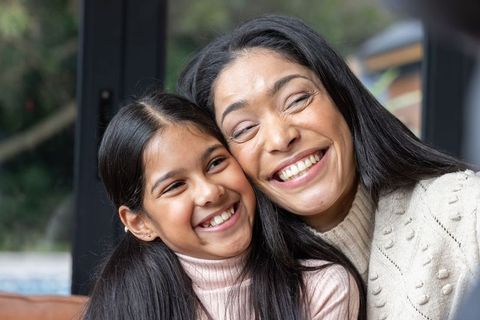 Mother and daughter sharing joyful cozy moment on couch smiling in knit sweater closeup