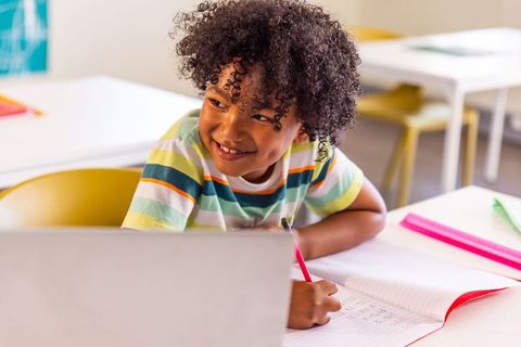 Smiling child writing while using laptop in colorful classroom