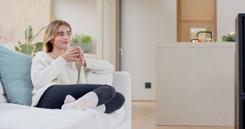 Woman Enjoying Warm Drink on Cozy White Sofa in Minimalist Home