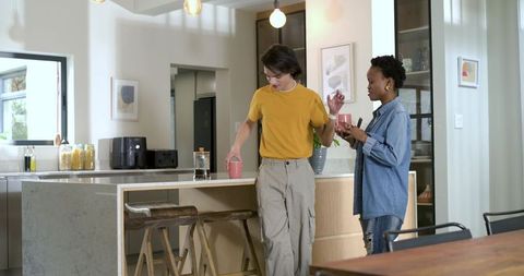 Diverse friends chatting over coffee at stone island in modern open-plan kitchen interior