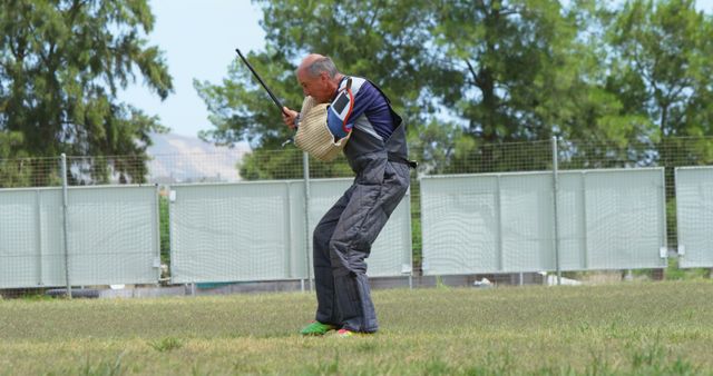 Senior man practicing kendo with a shinai in an outdoor grassy area surrounded by trees. He wears protective gear and appears focused. Suitable for topics related to martial arts, sports training, senior fitness, and outdoor activities.