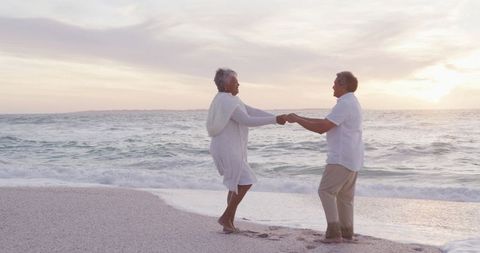 Senior couple dancing on serene beach at sunset in joyful harmony