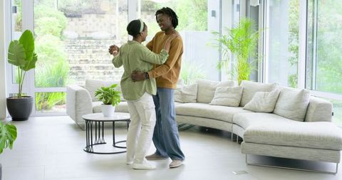 African American Couple Dancing in Sunlit Modern Living Room with Sectional Sofa