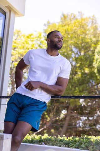 Mature african american man leaning on balcony railing wearing tee and teal shorts