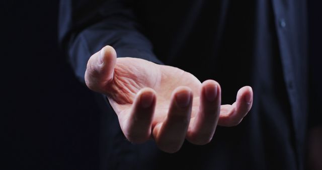 Hand shown in close-up with open palm reaching out on dark background. Useful for illustrating concepts of help, hope, assistance, invitation, or seeking aid. Ideal for use in motivational materials, support services campaigns, health sector communication, or community outreach promotions.