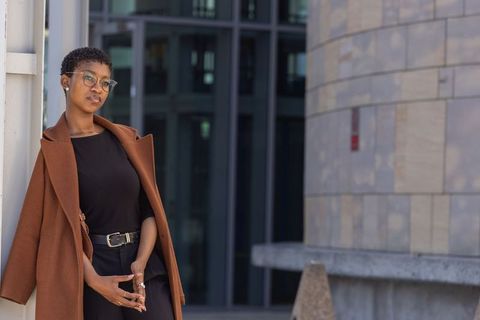 Confident african professional leaning against column wearing rust coat in modern plaza
