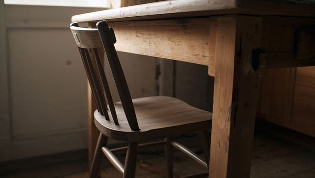 Rustic wooden chair tucked under worn farmhouse table with warm window light and patina