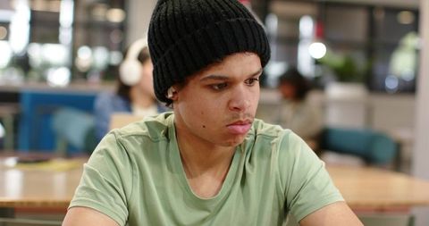 African american man wearing black beanie and earbud sitting focused in coworking cafe