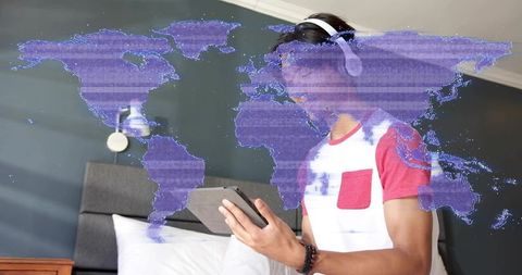 Teen wearing headphones using tablet with holographic world map overlay for study