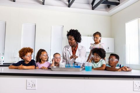 Diverse children exploring science with teacher demonstrating colorful test tube experiment
