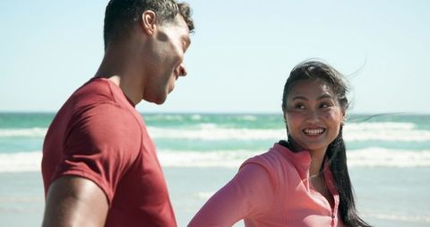 Sunlit Beach Couple Smiling in Athletic Wear by Ocean Waves, Happy Active Lifestyle